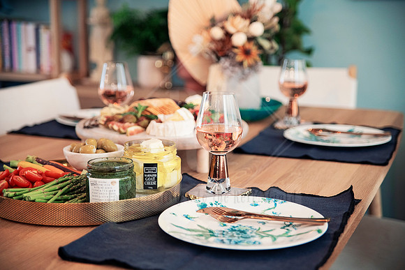 Close-up of artisan cheese board, dips, rosé, and fresh produce on a navy placemat.