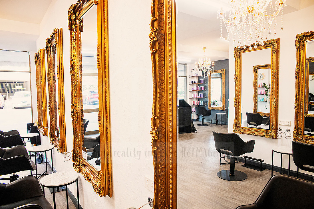 Salon interior with black chairs, chandelier, and wall lined with ornate gold mirrors.