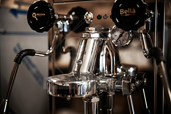 Close-up of industrial chrome espresso machine with Bella branding and dual spouts.