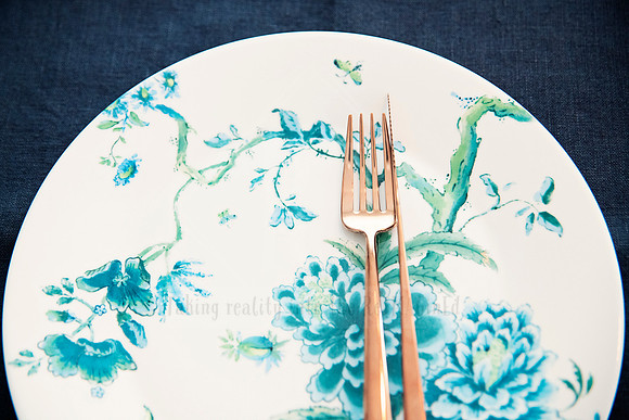 Close-up of botanical print plate with gold cutlery on navy placemat.