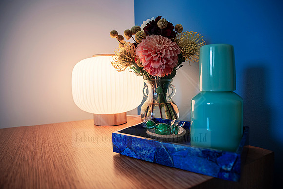 Soft glowing lamp on bedside with vibrant flowers in brass vase and sea glass bottles.