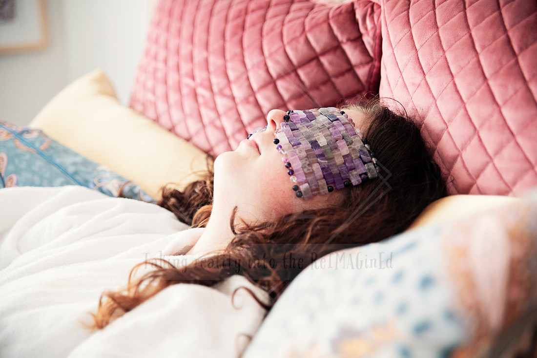 Woman lying in bed with a beaded lavender eye pillow during a relaxation moment.