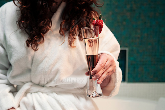 Guest in a white robe holding a glass of sparkling rosé with fresh strawberry garnish.