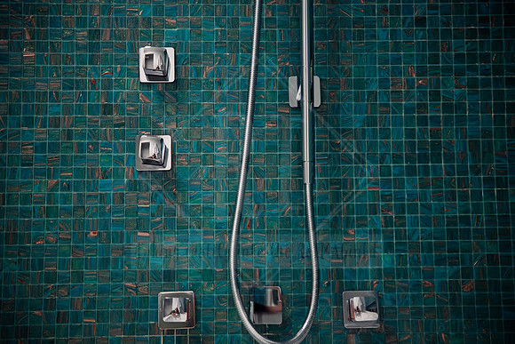 Modern rainfall shower and dual mixer heads against deep green bathroom mosaic tiles.