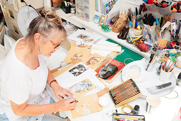 Mixed media artist creating layered works at busy desk, styled shoot for visual artist content package.