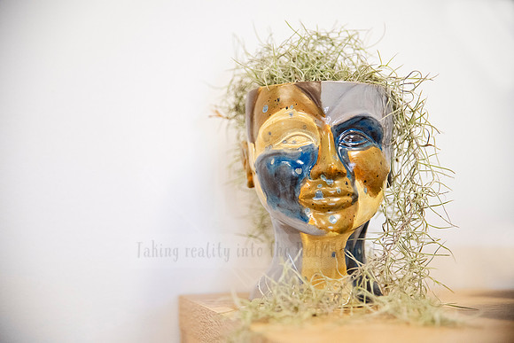 Gold and blue painted ceramic mask with moss detail, striking mixed media piece featured for Artwalk highlights.