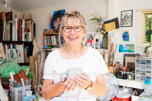 Portrait of artist smiling with mug in hand, photographed in studio for relaxed brand and website visuals.