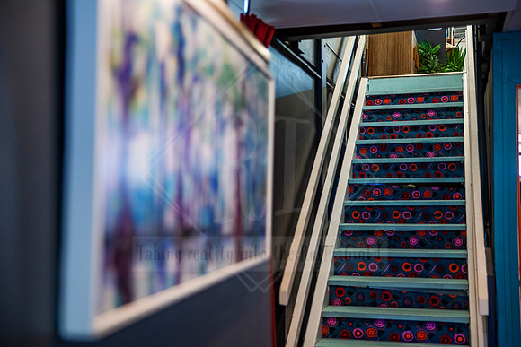 Framed artwork blurred in foreground, looking up at patterned stairwell inside Sunset Framing & Gallery.