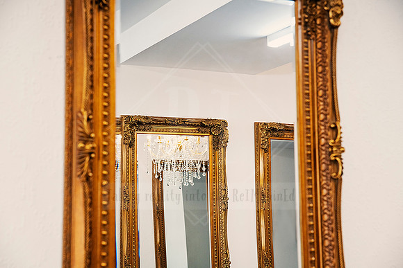 Reflection of ornate gold-framed mirrors in a chic white wall salon interior.