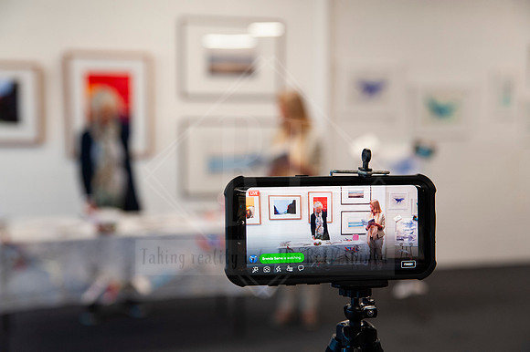 Behind-the-scenes photo of smartphone filming in gallery space, capturing real-time art showcase content.