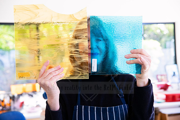 Playful image of artist holding up sheet of golden glass, part of Artwalk creative portrait series.