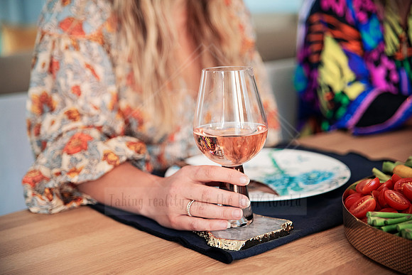 Close-up of rose wine glass held at a dining table with vibrant scarf and white blouse.