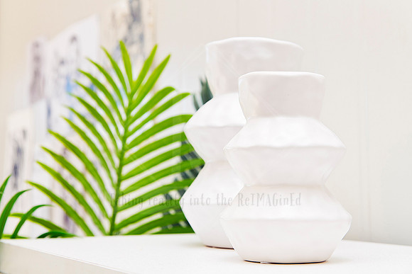 Bright studio shelf featuring white sculptural ceramics and a green palm leaf.